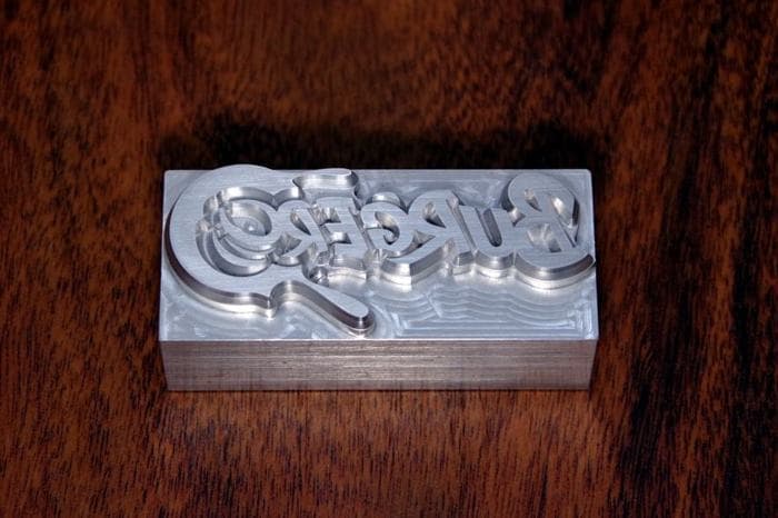 A CNC-machined aluminium stamp block with the Burgero logo in relief