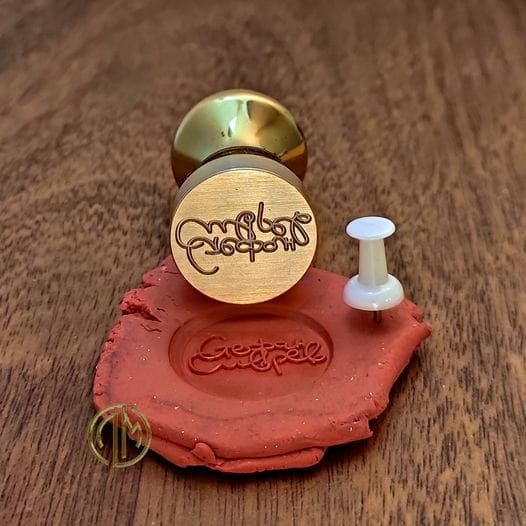 A polished brass seal stamp next to its red wax imprint