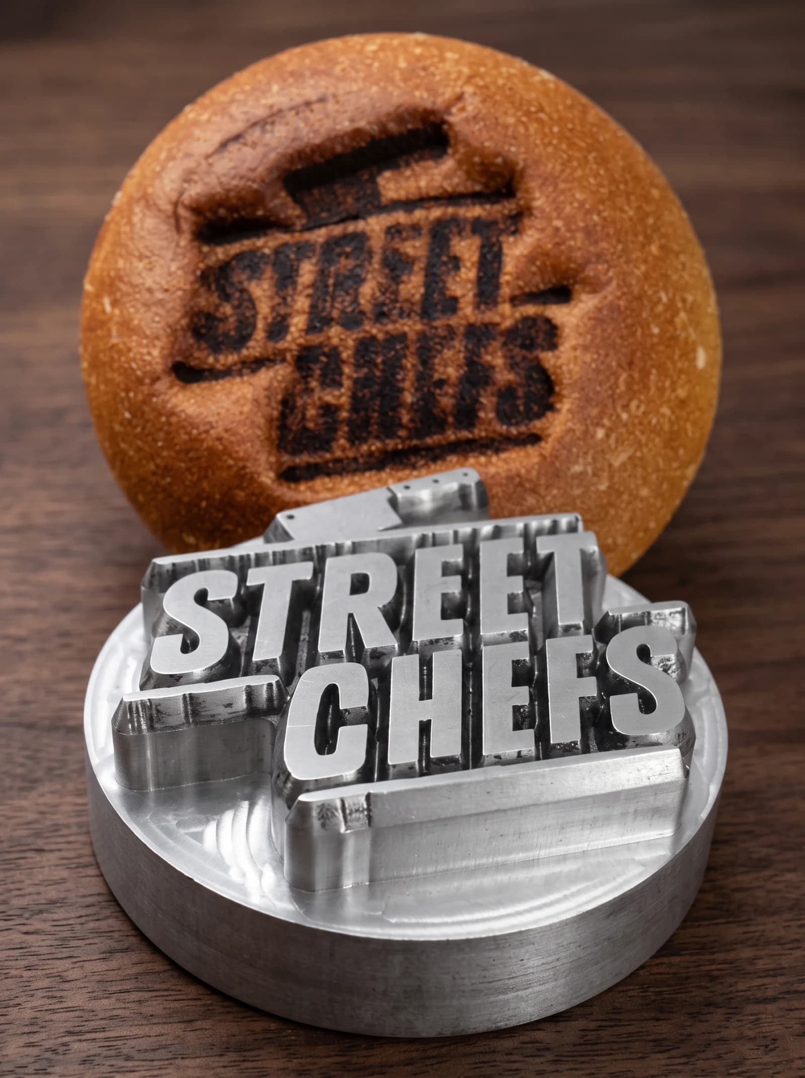 A CNC-machined metal branding stamp resting beside a burger bun branded with the Street Chefs logo